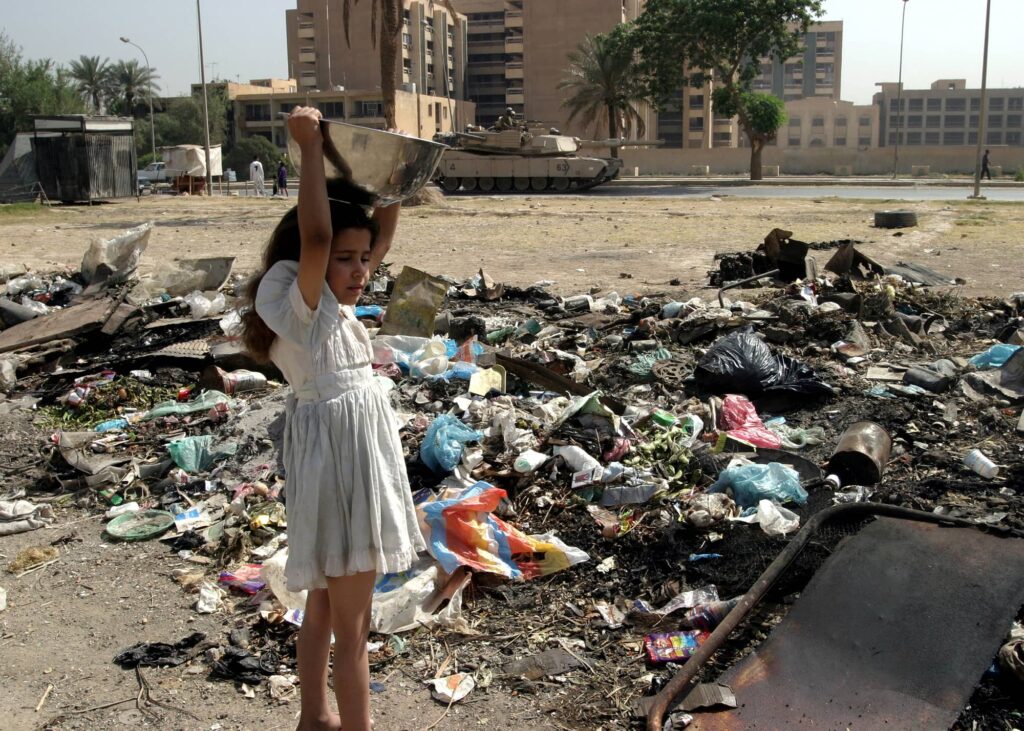 A young Iraqi girl prepares to dump trash in a pile of garbage on a Baghdad street, as basic needs like water and electricity are still scarce, May 2003. Photo credit: Reuters.