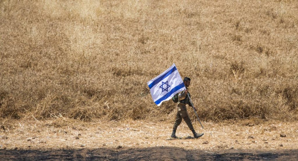 An IDF Soldier walks with the flag of Israel near the Gaza border. Photo credit: Ilia Yefimovich/dpa