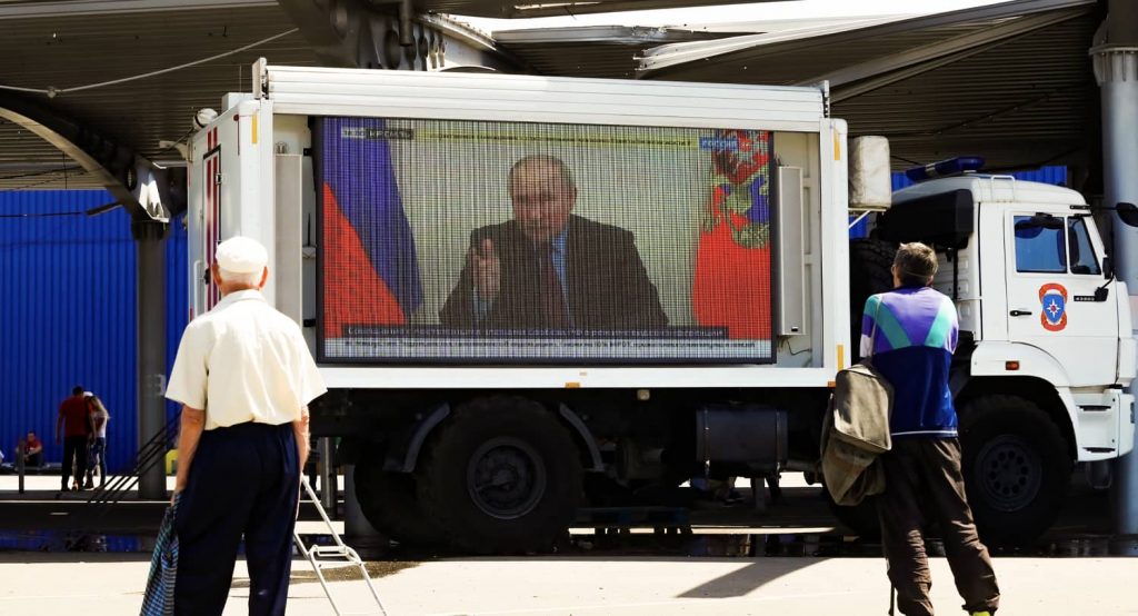 Russian President Vladimir Putin is seen on a screen broadcasting Russian TV news programs in Mariupol. Photo credit: REUTERS/Alexander Ermochenko