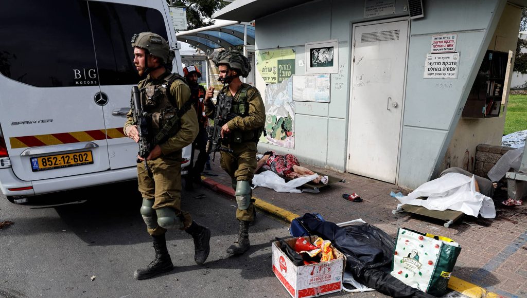 Israeli soldiers walk past the bodies of people that lie on a street after they were killed by Hamas gunmen from Gaza, in Sderot, southern Israel October 7, 2023. photo credit: REUTERS/Ammar Awad