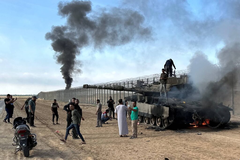 Palestinians and a burned Israeli military vehicle at the Gaza border, October 7, 2023. Photo credit: REUTERS/Mohammed Fayq Abu Mostafa.